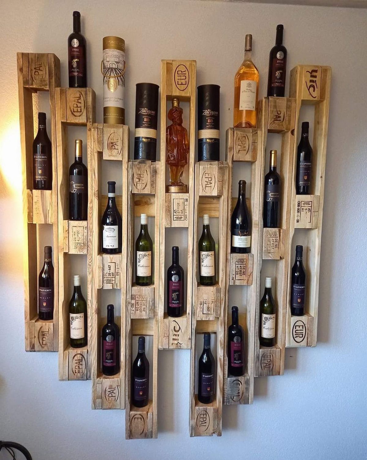 22 French Country Dining Room Ideas with Rustic Charm 9 Wooden pallet wine rack mounted on a white wall holding various wine bottles.