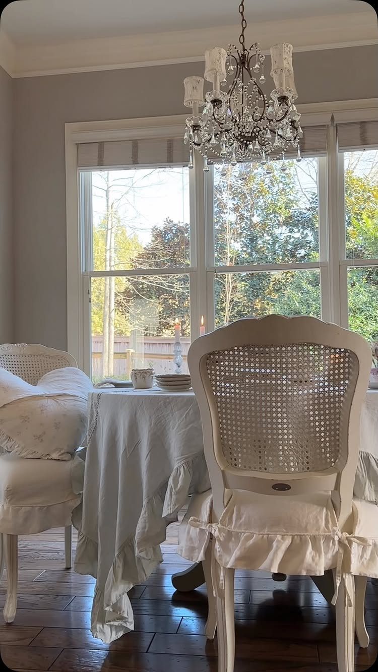 22 French Country Dining Room Ideas with Rustic Charm 16 White cane-back chairs and a ruffled table under a crystal chandelier in a dining room.