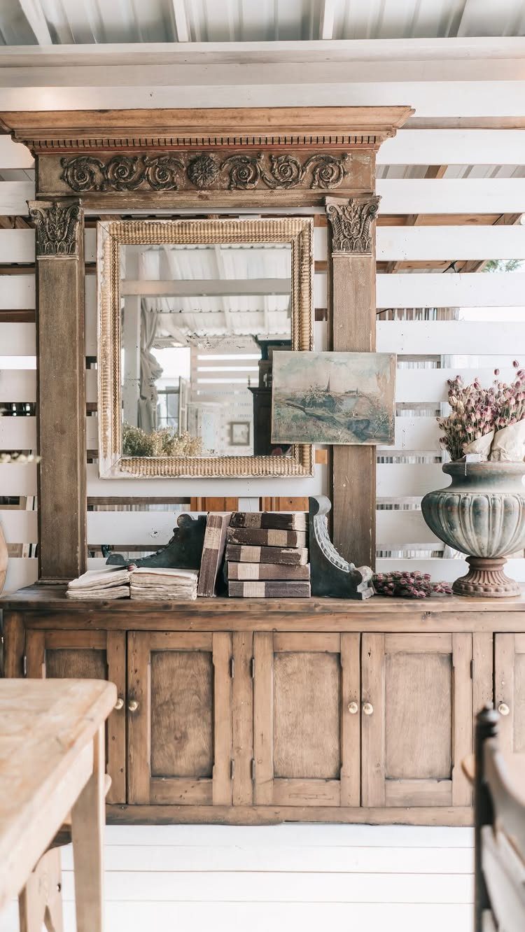 22 French Country Dining Room Ideas with Rustic Charm 4 Ornate vintage mirror with carved wooden frame resting on a rustic wooden sideboard.