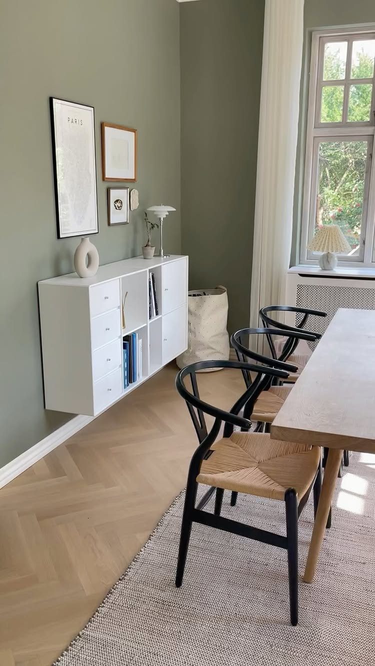 11 Green Painted Dining Room Ideas with Photos 8 Sage green dining room with a wooden table, black chairs, and white sideboard.