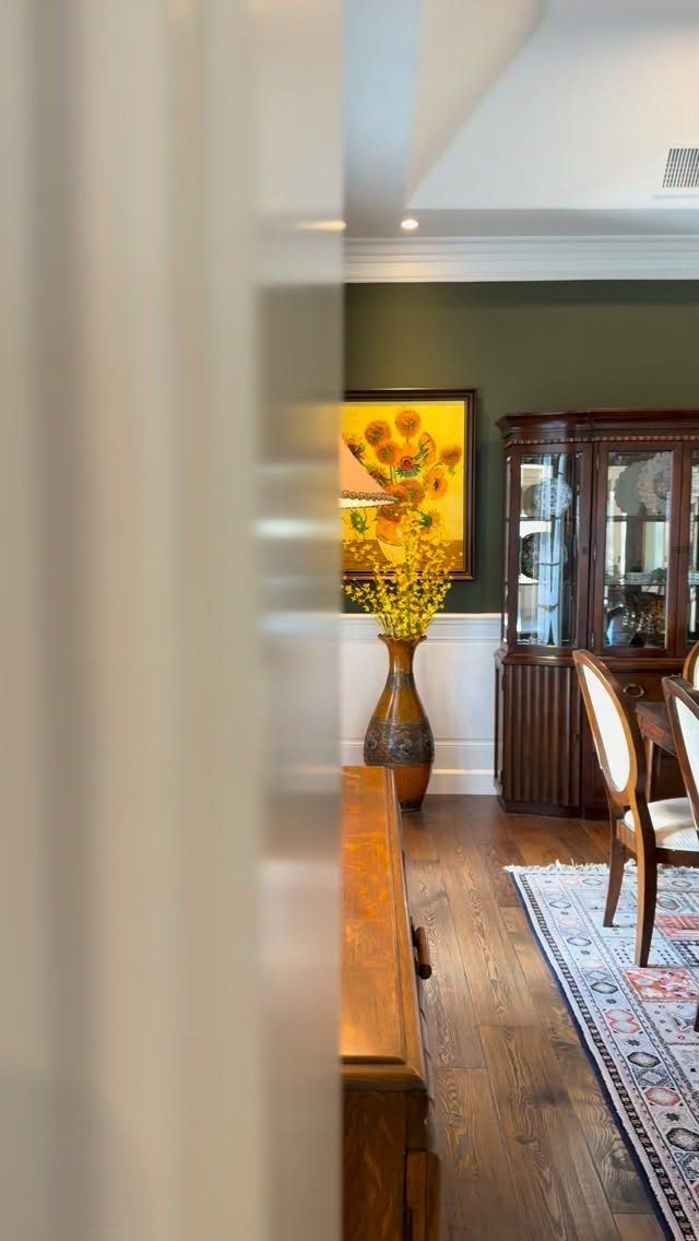 9 Green Walls for Dining Room Ideas with Photos 1 Dark green walls in a dining room with white wainscoting and wooden furniture.