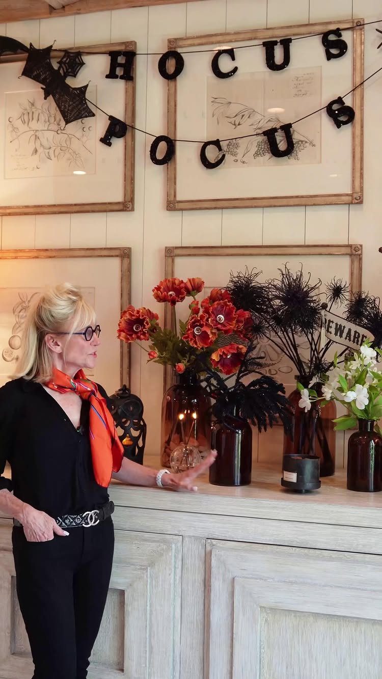 16 Halloween Room Decor Ideas to Set the Scene 9 Woman standing next to brown vases with orange flowers and black spooky stems.