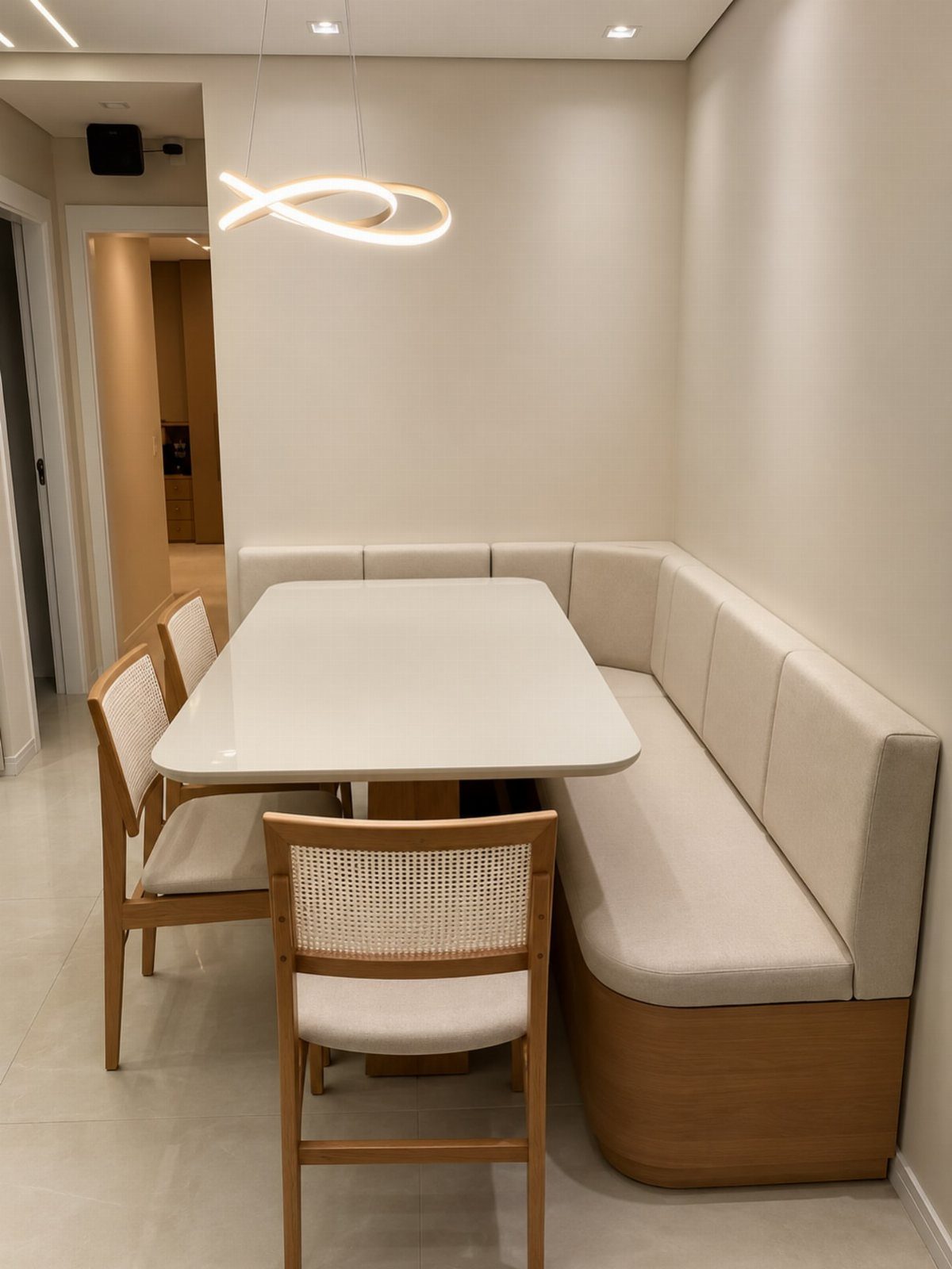 L-shaped cream upholstered dining bench and white table with wooden cane-back chairs.