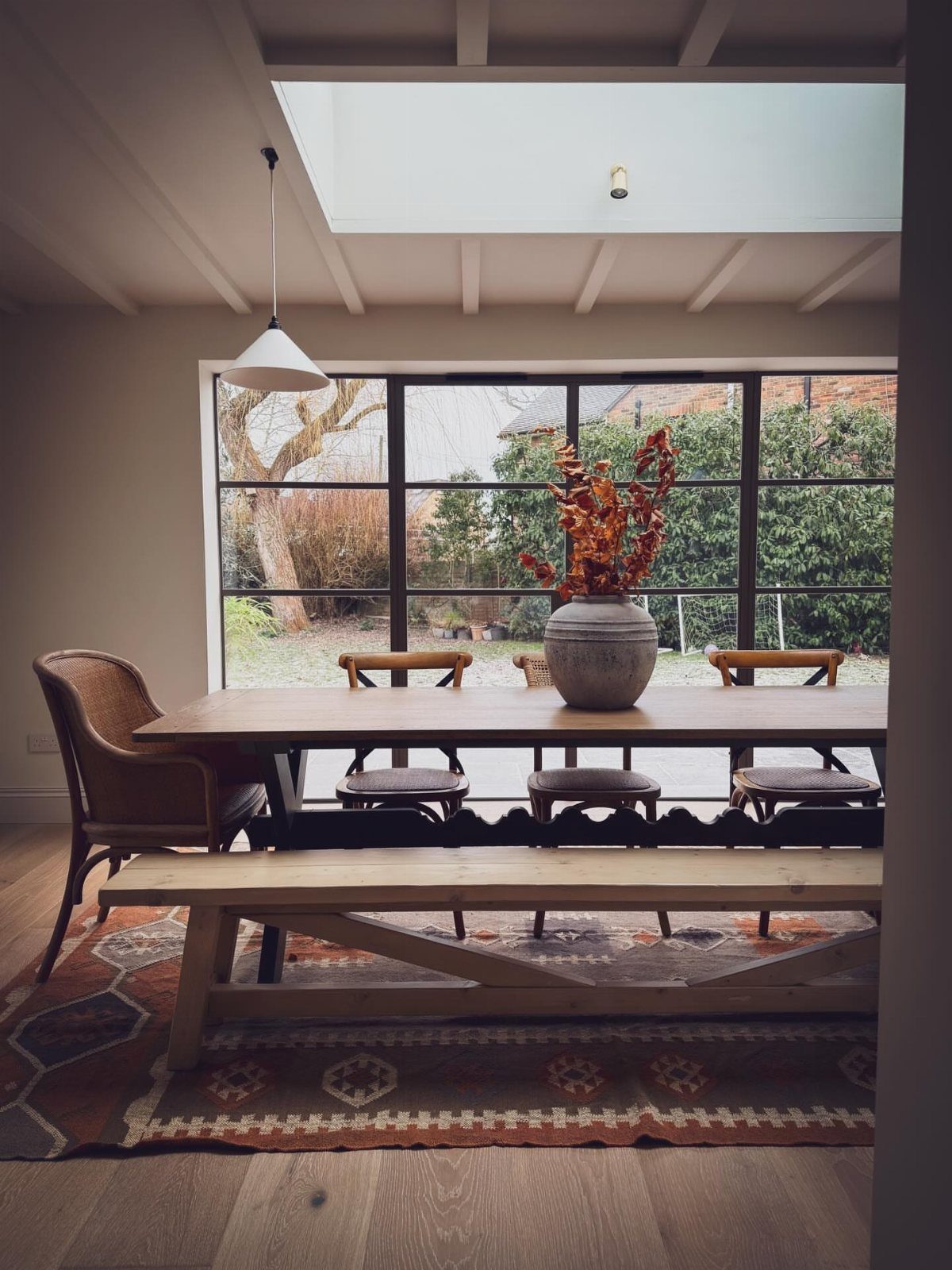Wooden dining table with a bench and mixed chairs in a bright room.