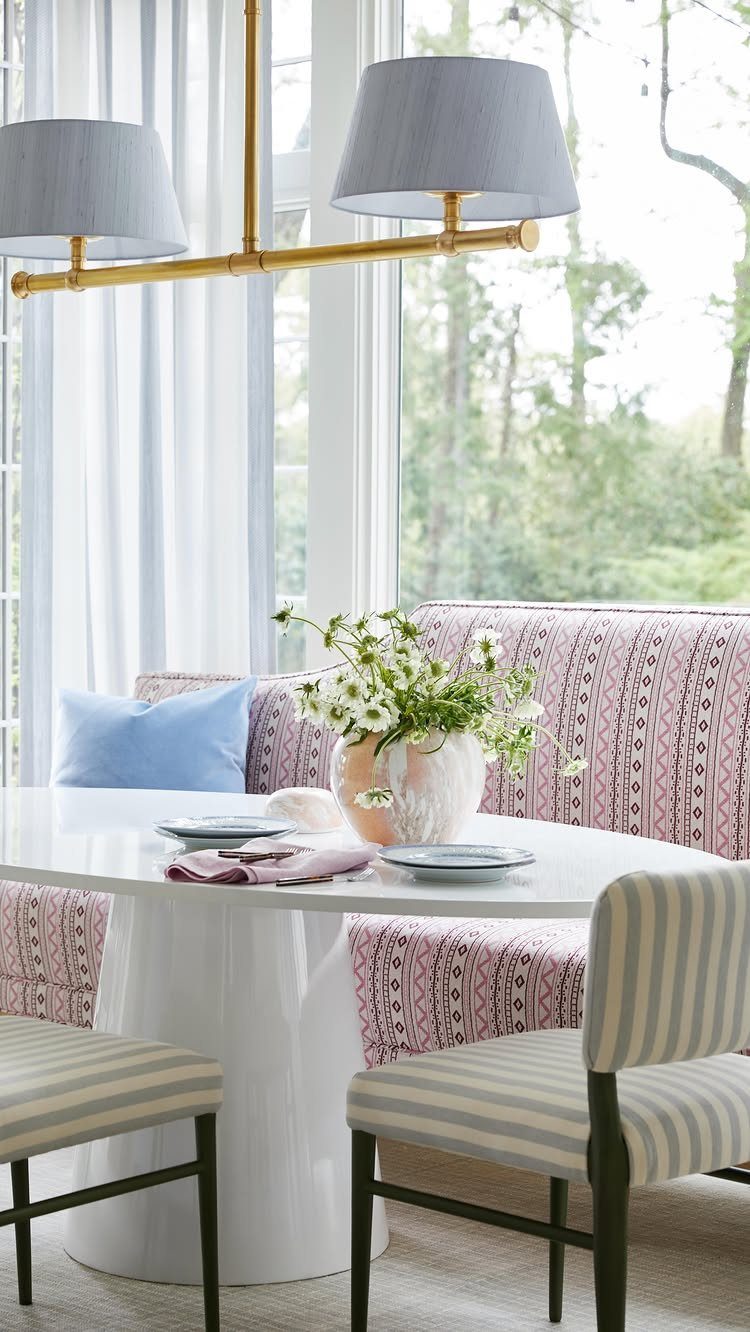 12 Living Dining Room Decor Ideas for Combined Spaces 4 White oval dining table with a pink patterned banquette and striped chairs.