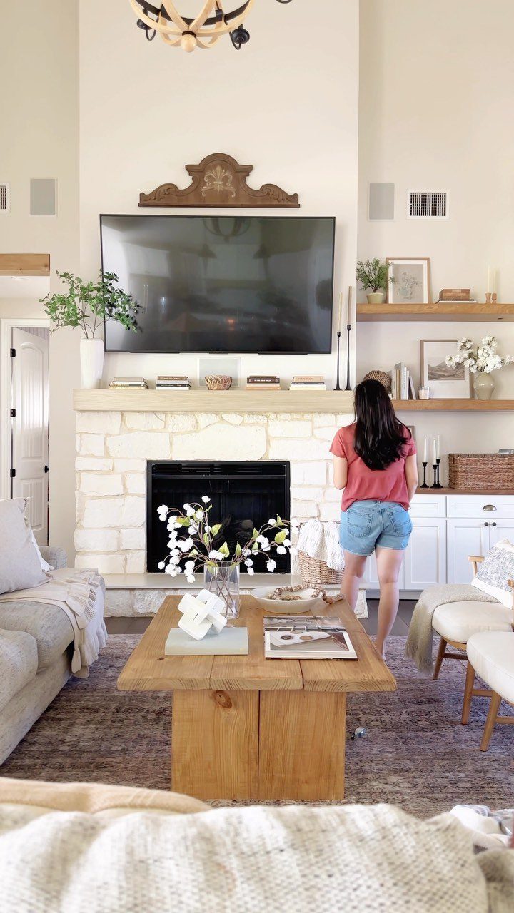Stone fireplace with a decorated wooden mantel and television in a bright living room.