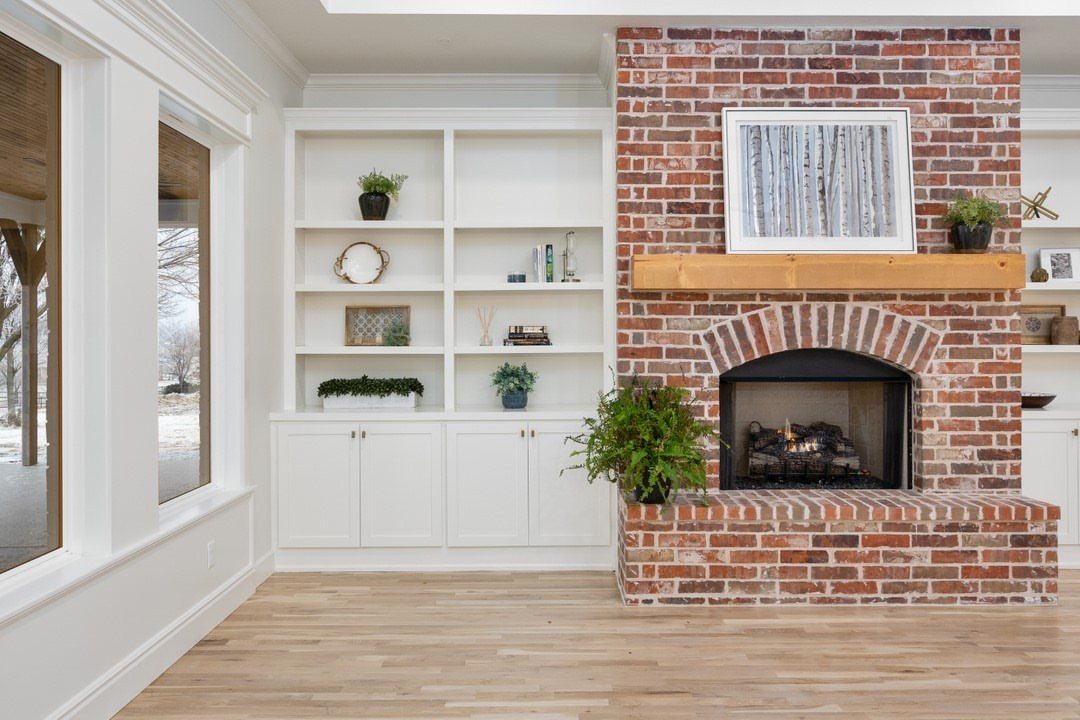 Red brick fireplace with a light wood mantel and white built-in shelving.
