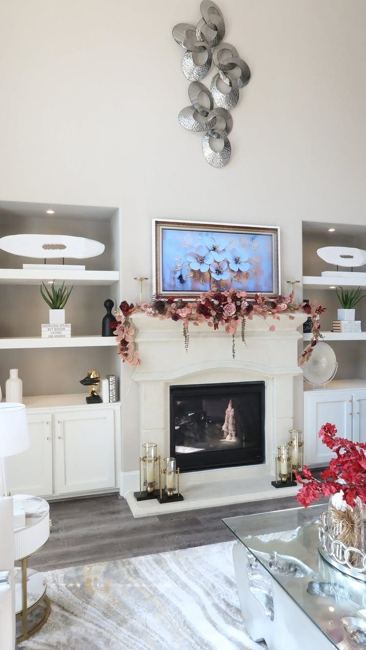 White fireplace mantel decorated with floral garland, painting, and silver wall sculpture.