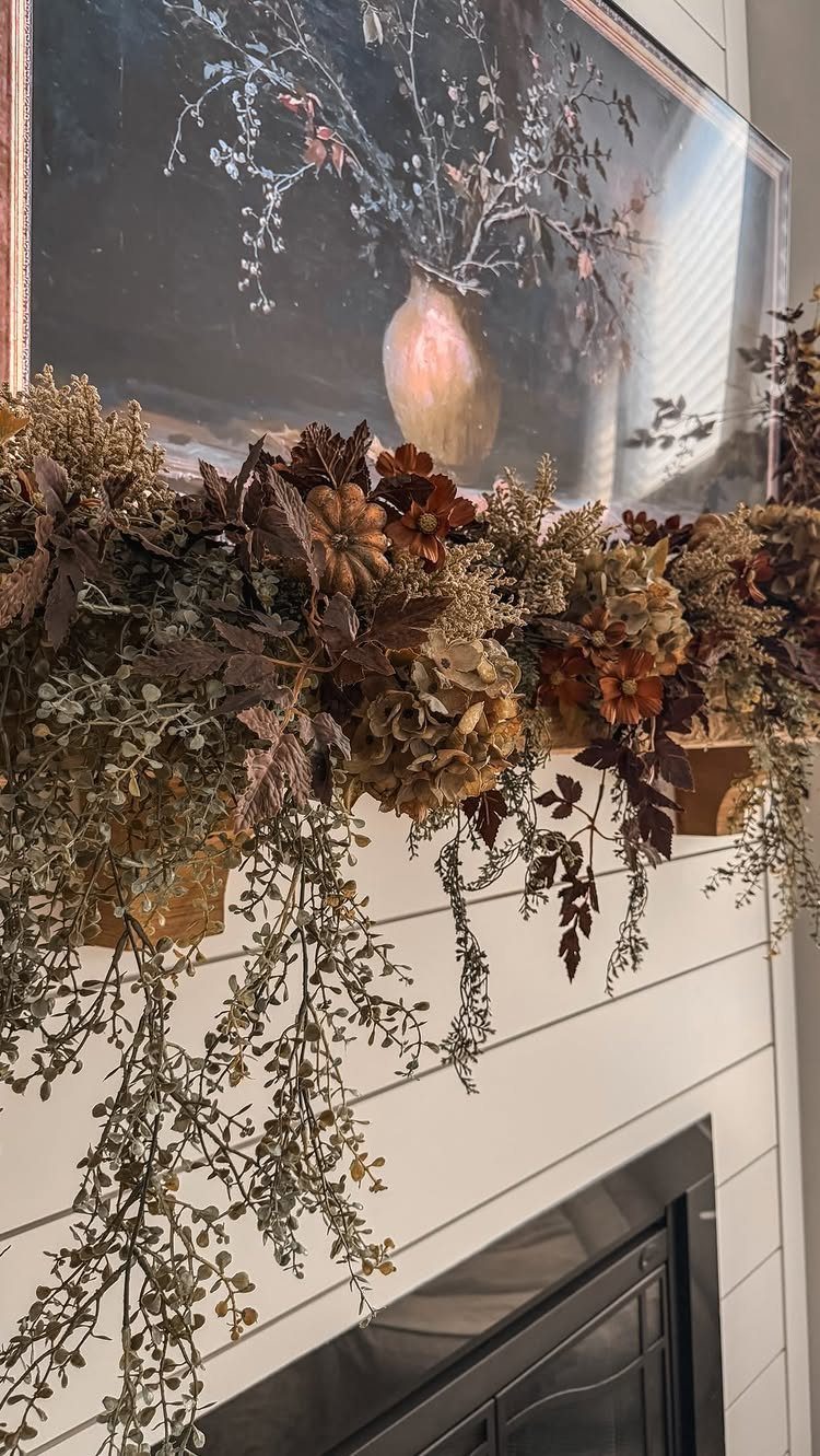 Autumnal garland with dried leaves and flowers decorating a white shiplap fireplace mantel.