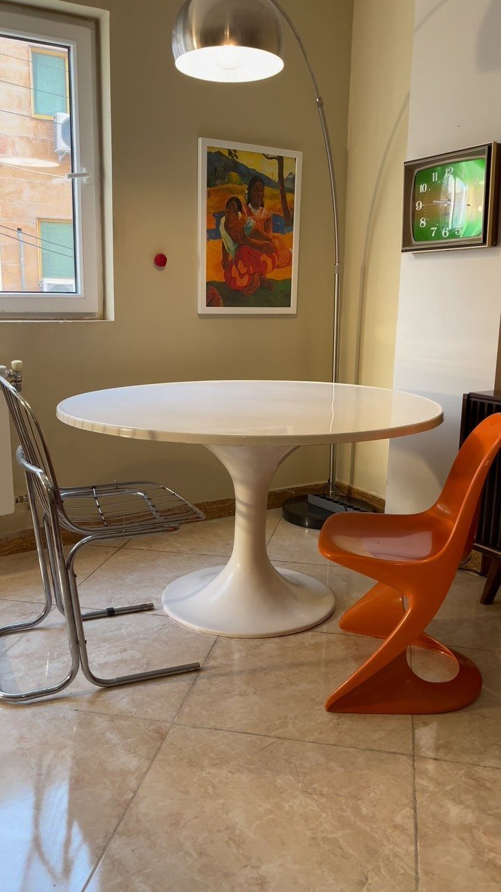 White tulip dining table with an arched silver floor lamp and colorful chairs.