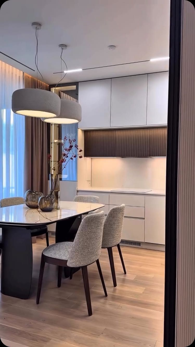 Two grey drum pendant lights hanging over a marble dining table in a modern room.