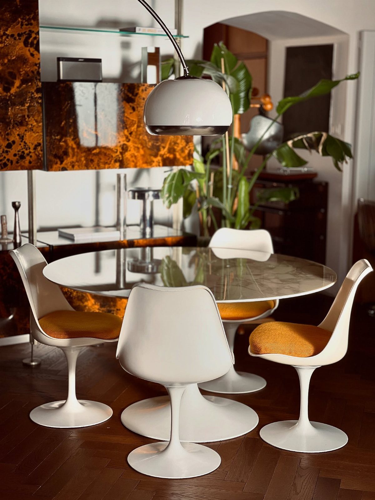 White dome pendant light over a glass table with white tulip chairs.