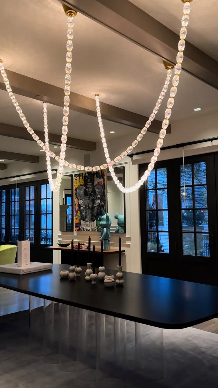 Draped crystal bead chandelier hanging over a modern black dining table in a room.