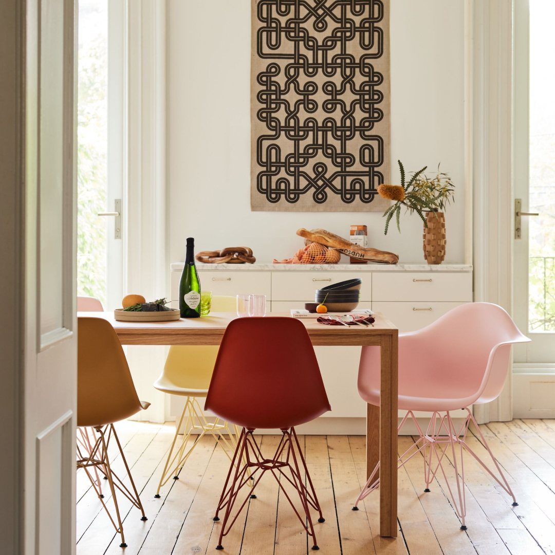 Colorful molded plastic chairs around a light wood dining table in a bright room.