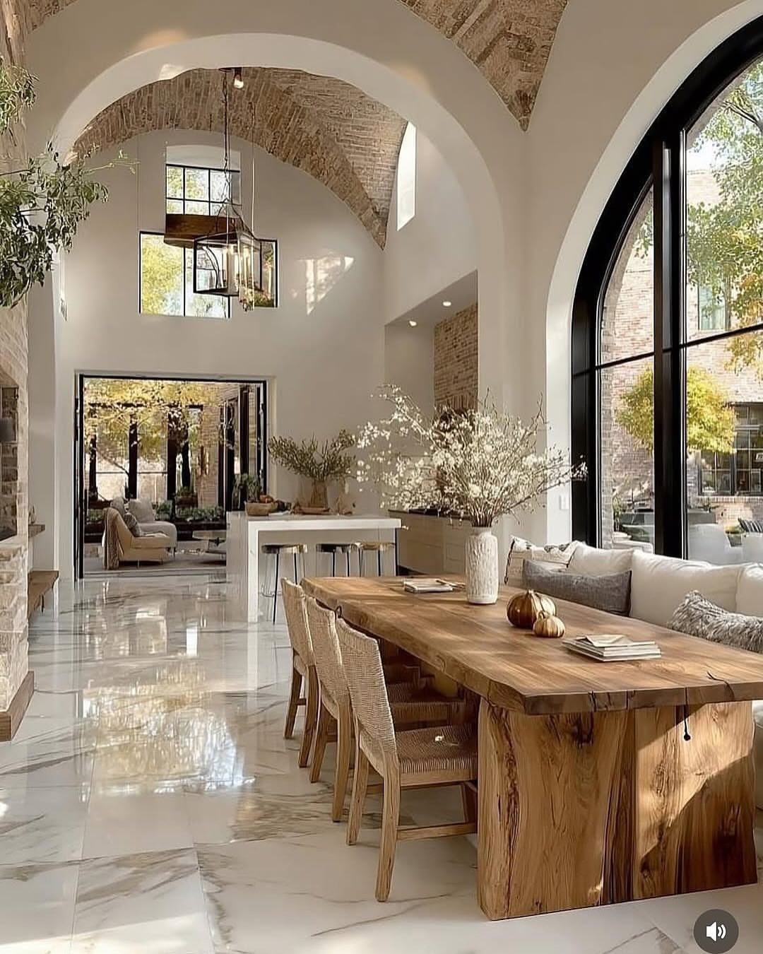 Live-edge wooden dining table with woven chairs in a bright, vaulted white room.