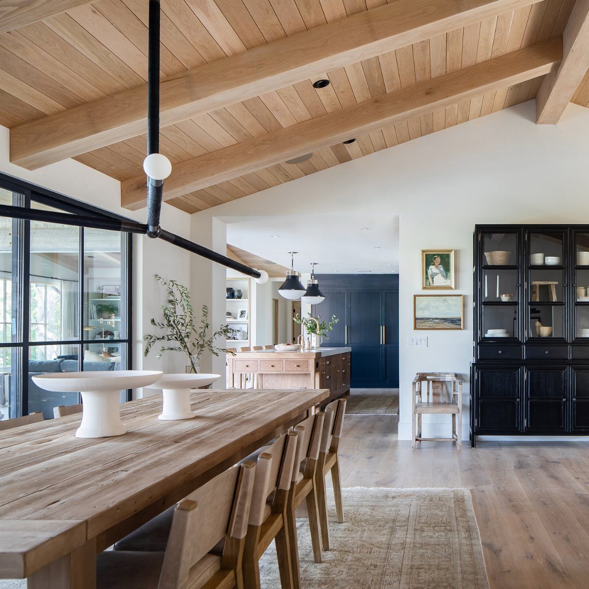 14 Modern Farmhouse Dining Room Ideas with Style 8 Rustic wooden dining table and chairs under exposed beams with modern black lighting.