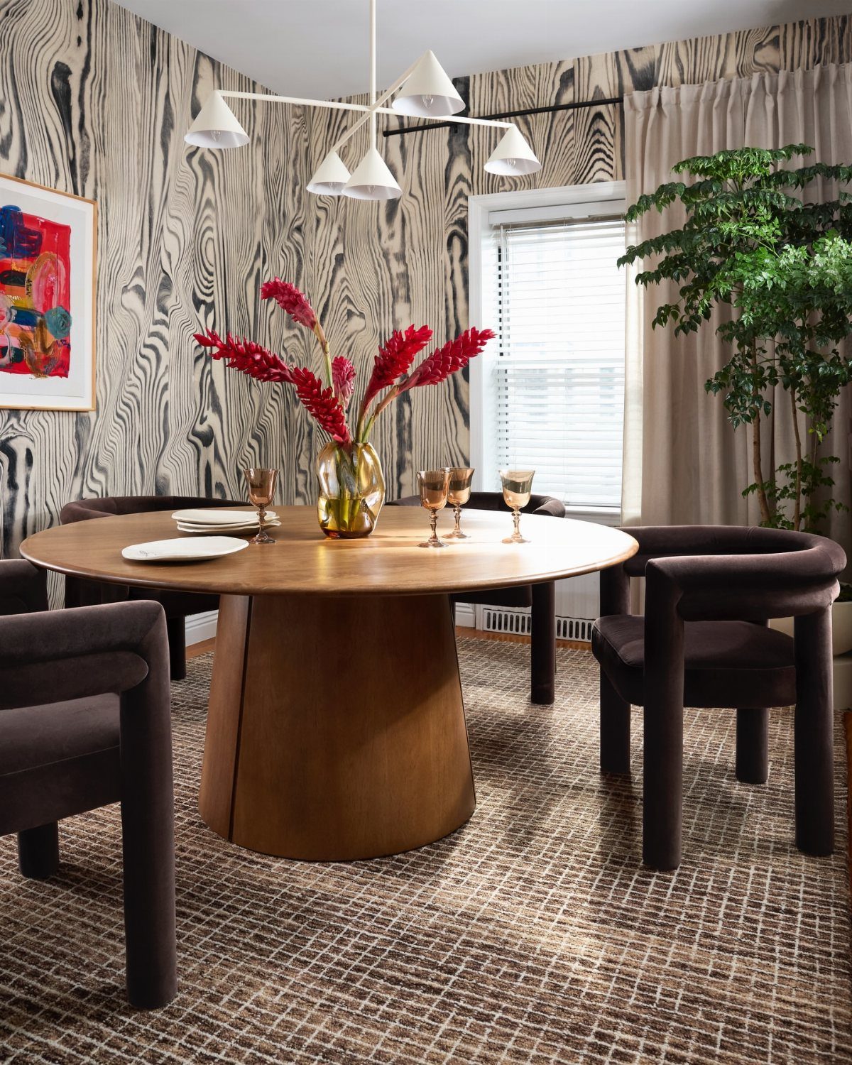 23 Modern Luxury Dining Room Ideas with Photos 7 Round wooden dining table with dark chairs against bold wood-grain wallpaper and modern lighting.