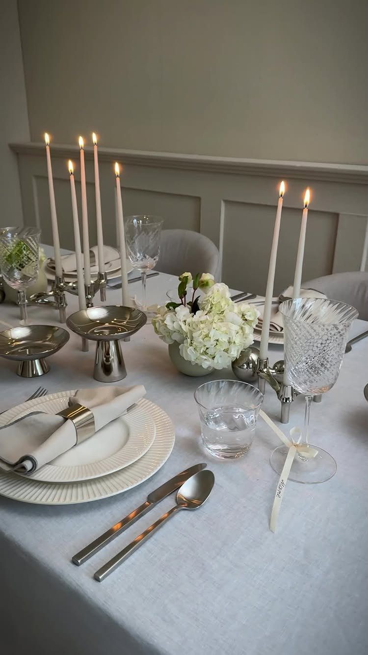 Dining table set with white linens, silver cutlery, taper candles, and white flowers.