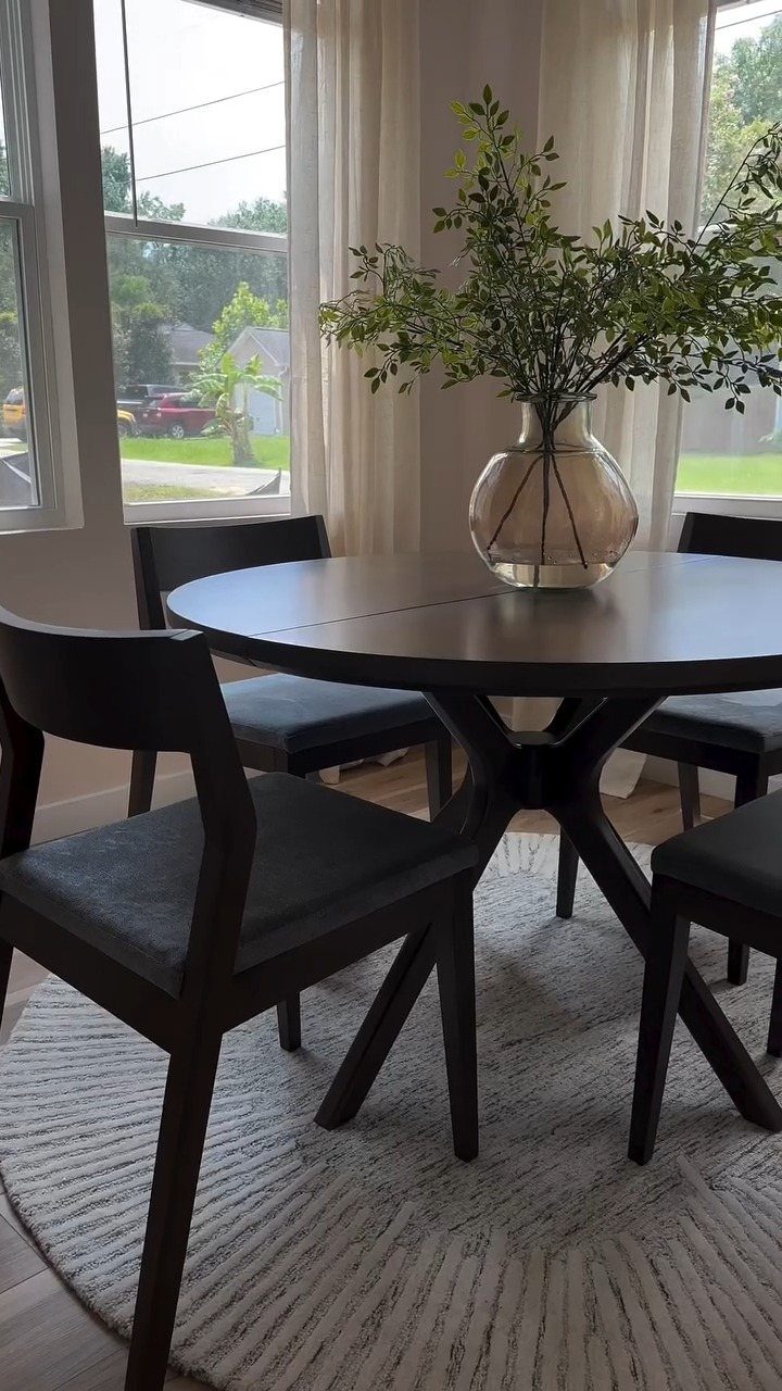 Round dark wood dining table with chairs and a plant on a white rug.