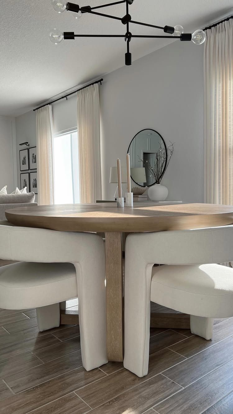 Round wooden dining table with white chairs and a single plant in a vase.