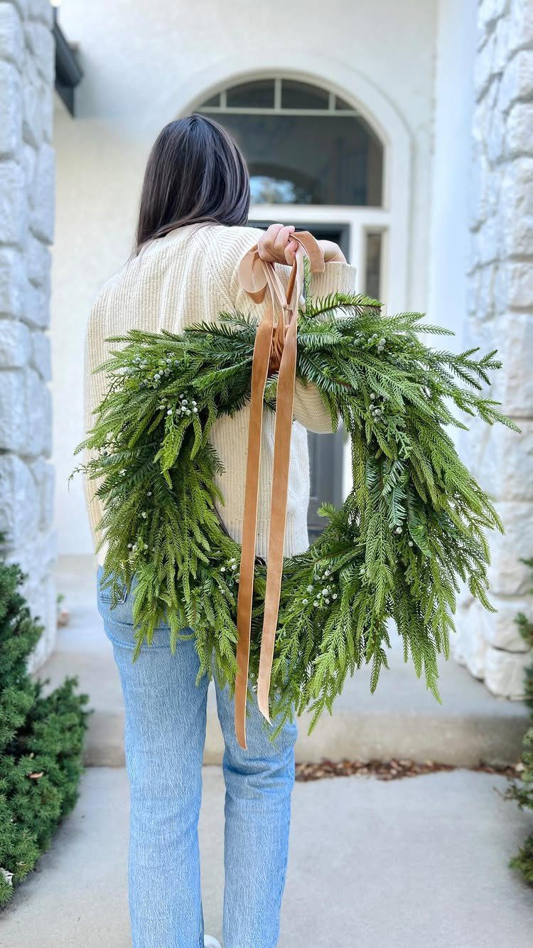 10 Neutral Color Christmas Decor Ideas for a Cozy Home 5 Green evergreen wreath with a long tan ribbon held by a person.