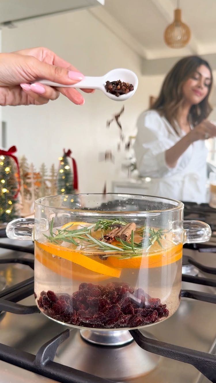 10 Neutral Color Christmas Decor Ideas for a Cozy Home 4 Cloves being added to a stovetop pot simmer with oranges, rosemary, and cranberries.