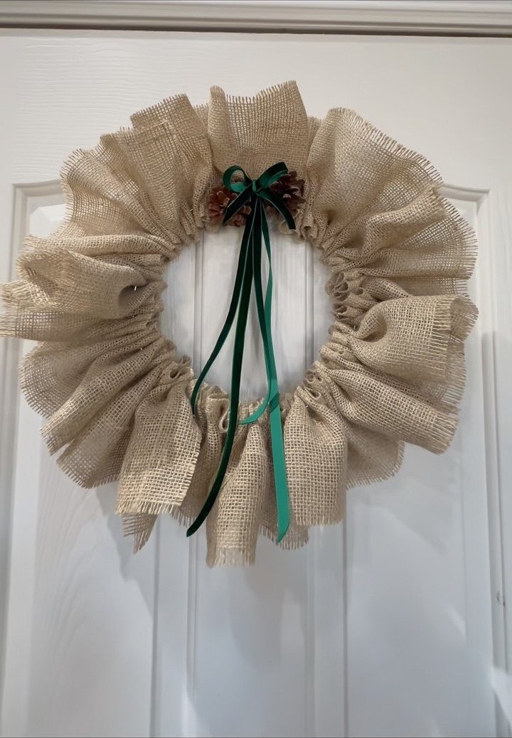 29 New Ideas for Christmas Decorating to Try in 2026 28 Burlap ruffled wreath with a green ribbon bow hanging on a white door.