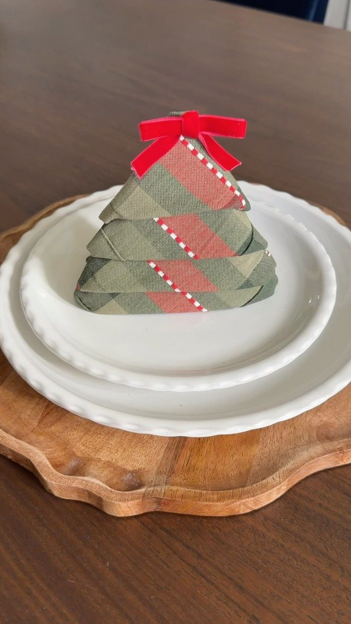 29 New Ideas for Christmas Decorating to Try in 2026 25 Folded Christmas tree napkin with red bow on white plates and wooden charger