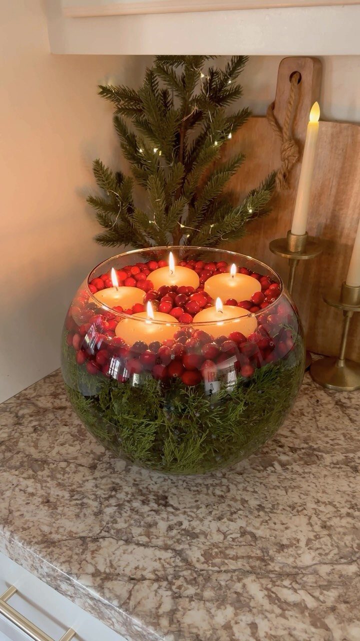 29 New Ideas for Christmas Decorating to Try in 2026 19 Glass bowl filled with green pine and red cranberries with floating candles.