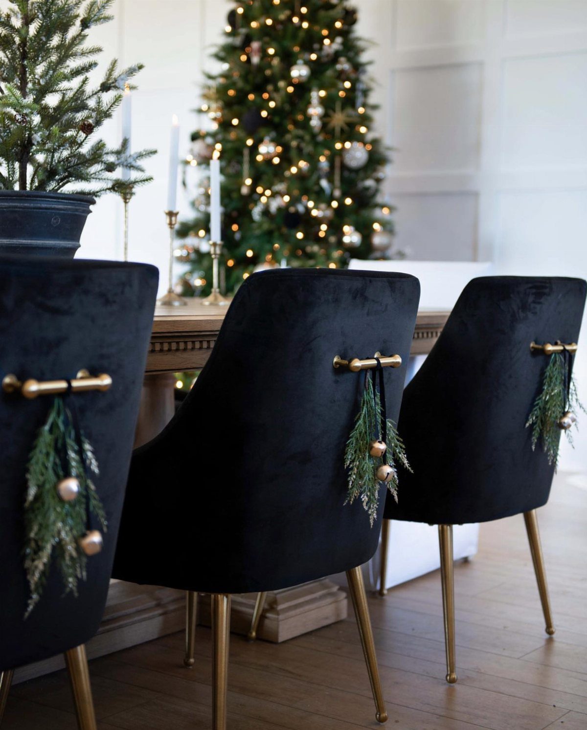 29 New Ideas for Christmas Decorating to Try in 2026 18 Black velvet dining chairs decorated with evergreen sprigs and gold ornaments on the backs.