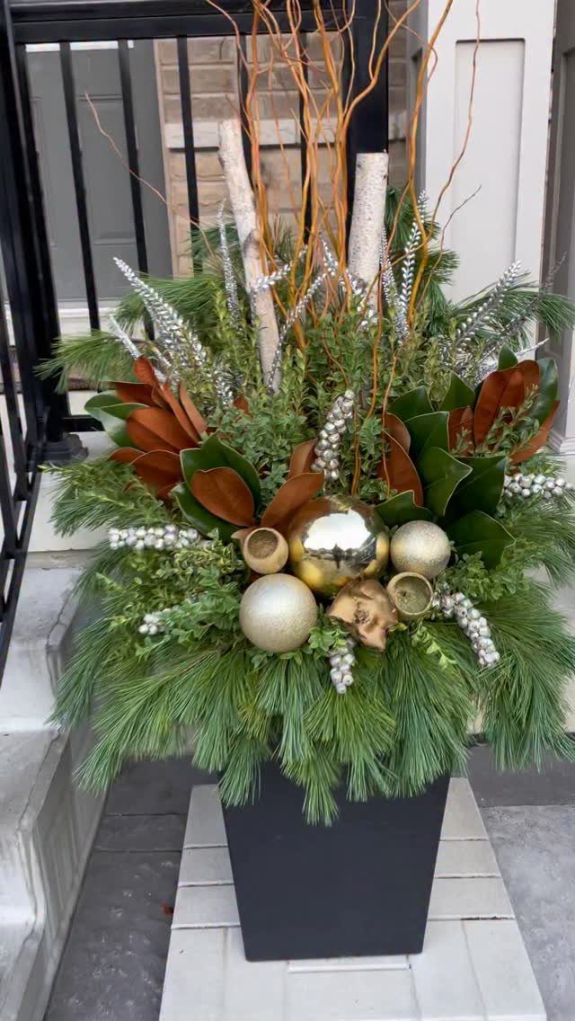 29 New Ideas for Christmas Decorating to Try in 2026 10 Holiday greenery arrangement with gold ornaments and birch branches in a black planter.