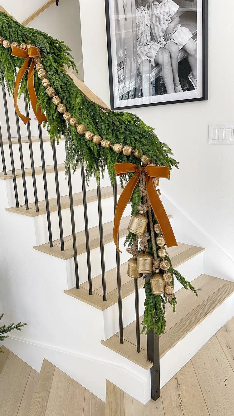 29 New Ideas for Christmas Decorating to Try in 2026 13 Layered evergreen and gold beaded garlands draped over a white staircase railing with bows.