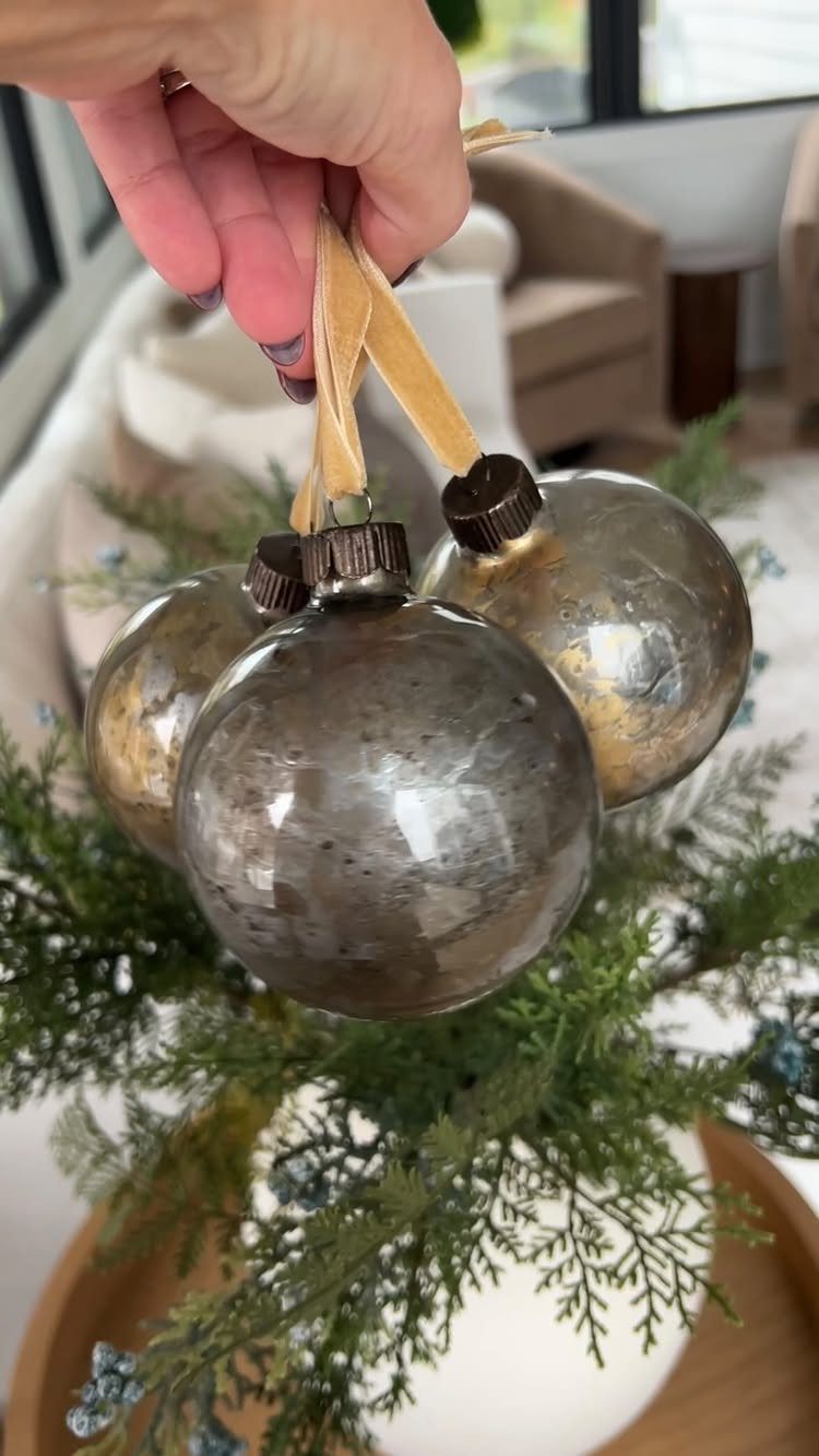 29 New Ideas for Christmas Decorating to Try in 2026 16 Silver metallic Christmas ornaments tied with gold ribbon over evergreen branches in a vase