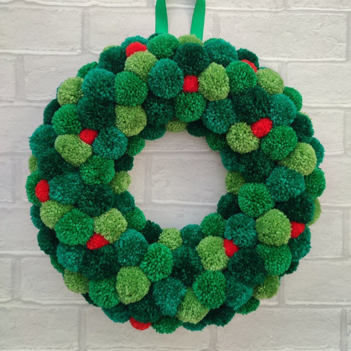 29 New Ideas for Christmas Decorating to Try in 2026 24 Yarn pom pom wreath in shades of green and red on white brick wall