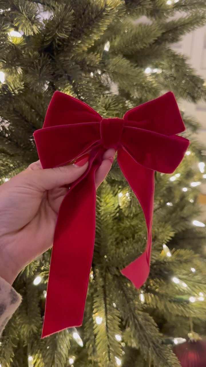 29 New Ideas for Christmas Decorating to Try in 2026 17 Red velvet bow held in front of a lit green Christmas tree.