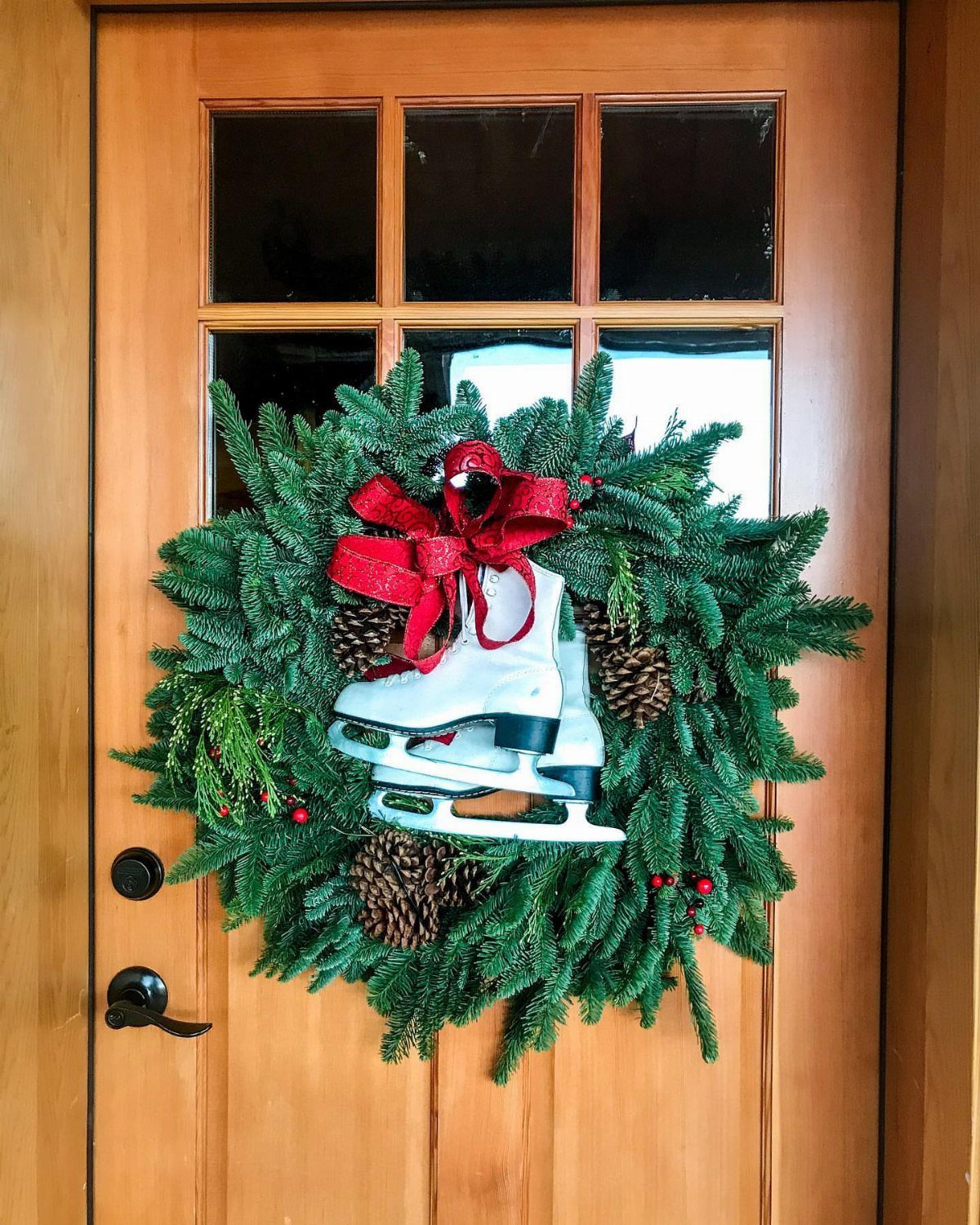 29 New Ideas for Christmas Decorating to Try in 2026 11 White ice skate and red bow decorating a green evergreen wreath on a wooden door.