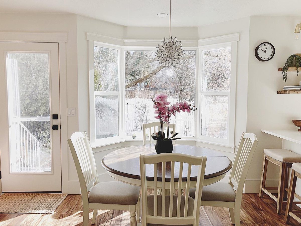 Round wooden dining table with white chairs in a bright, open dining area.