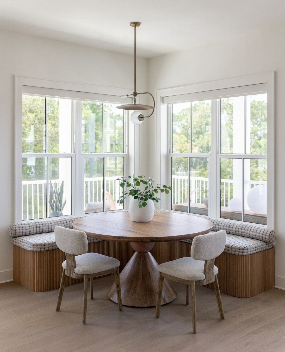 Round wooden dining table with checkered banquette seating and light grey chairs in nook.