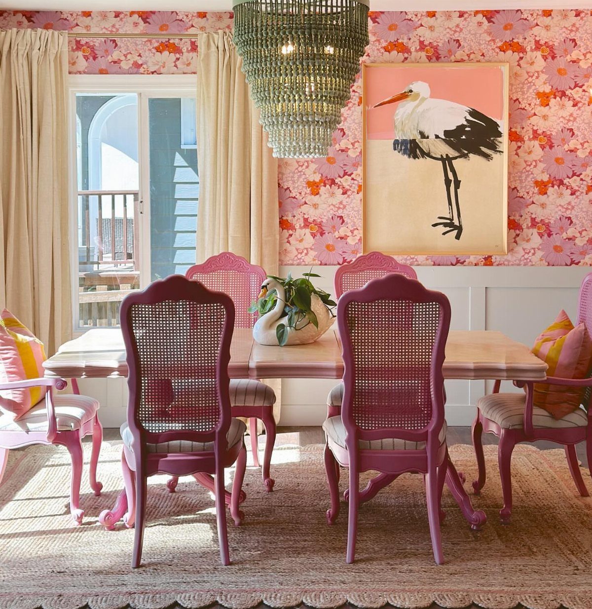 Dining room with bold pink floral wallpaper, magenta chairs, and a crystal chandelier.