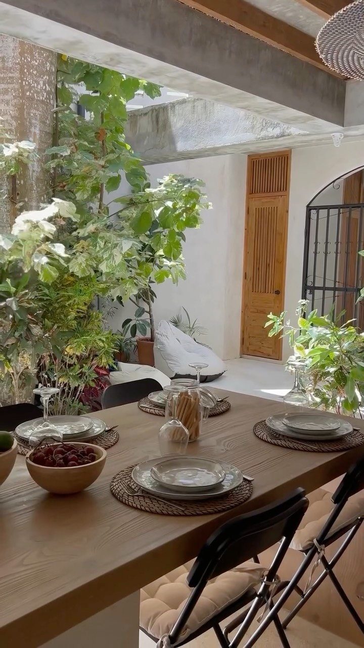 Wooden dining table set with plates and bowls in a bright, plant-filled patio area.
