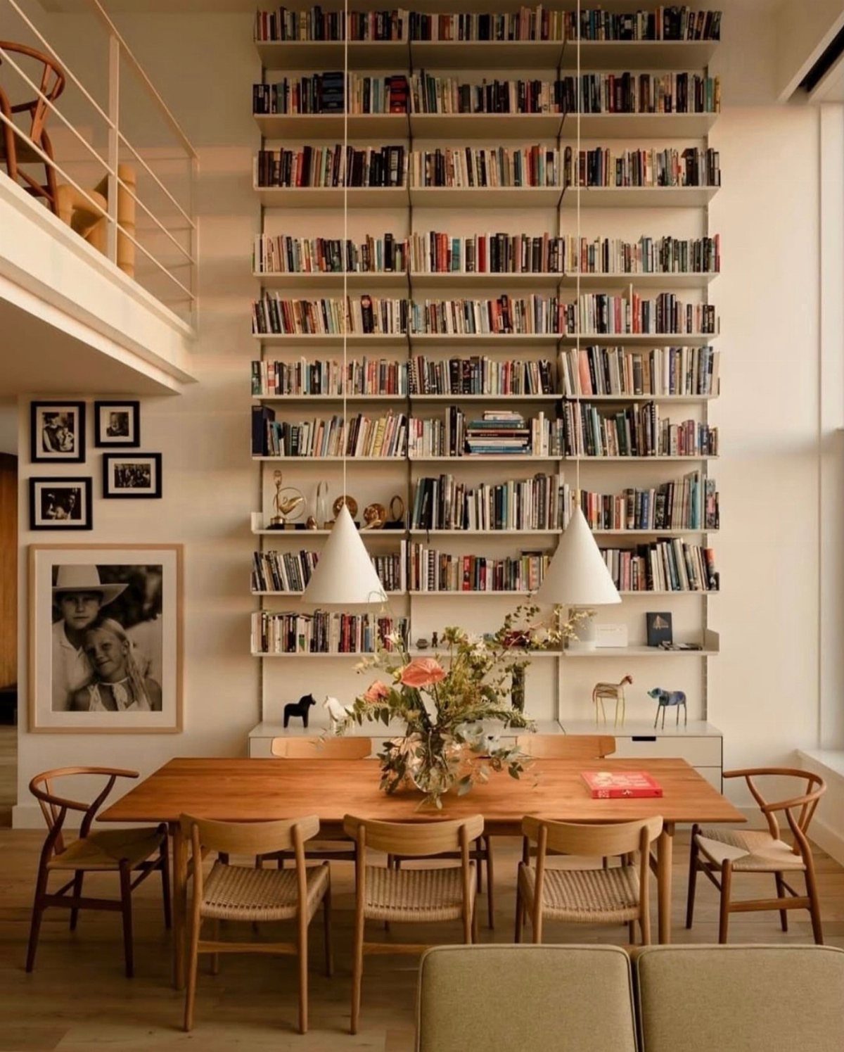 Wooden dining table and chairs set against a wall of tall open bookshelves.
