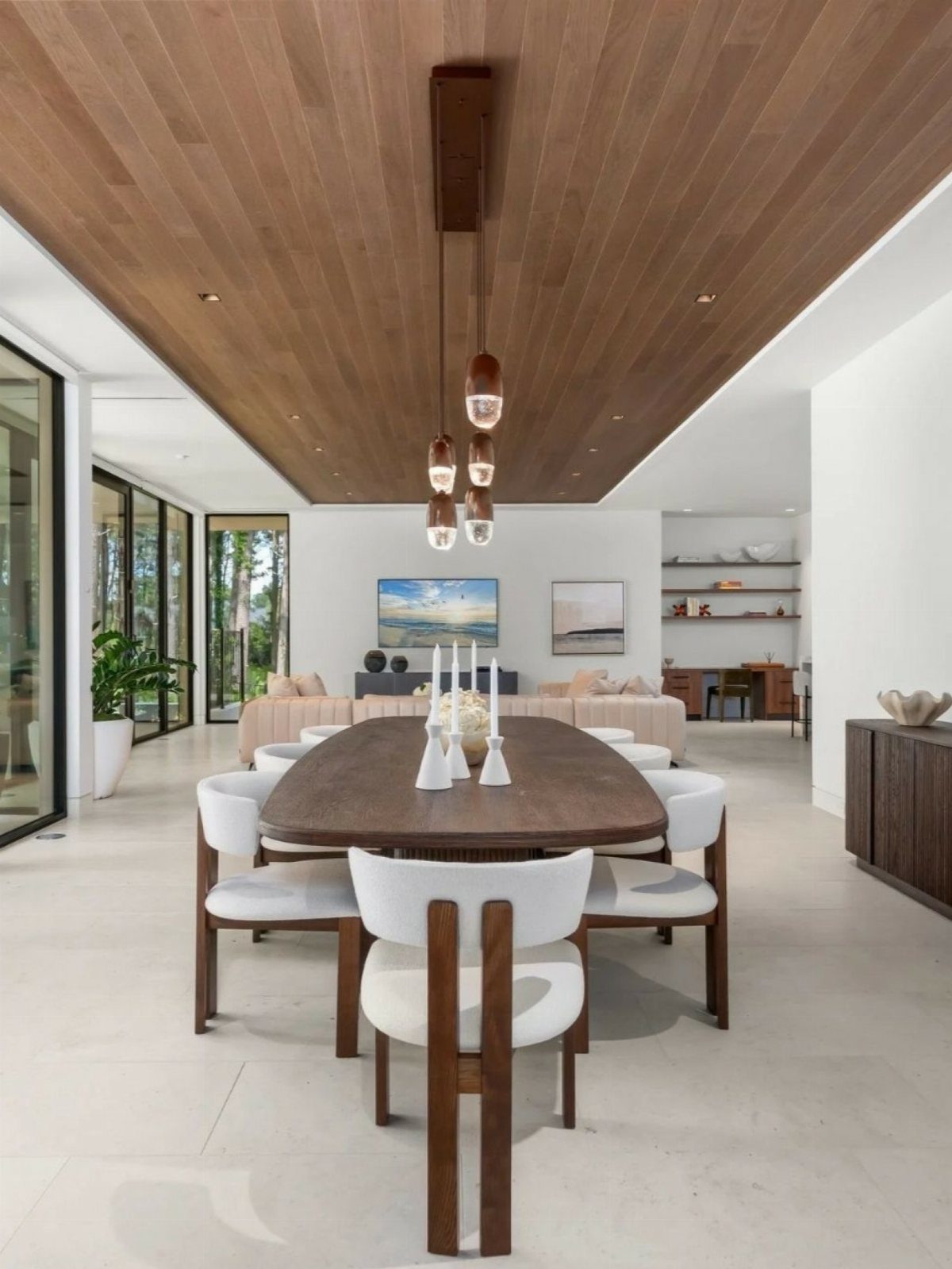 Oval wooden dining table with white chairs under a cluster of pendant lights.