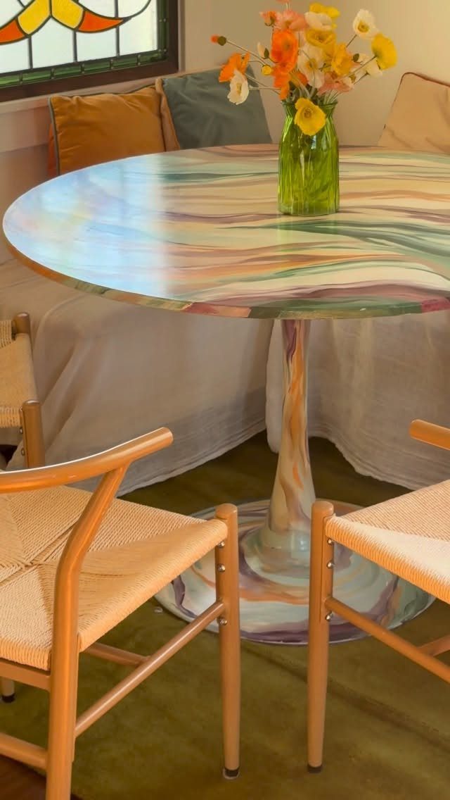 5 Painted Dining Room Table Ideas with Photos 5 Round dining table with colorful swirling paint, accompanied by woven chairs and fresh flowers.