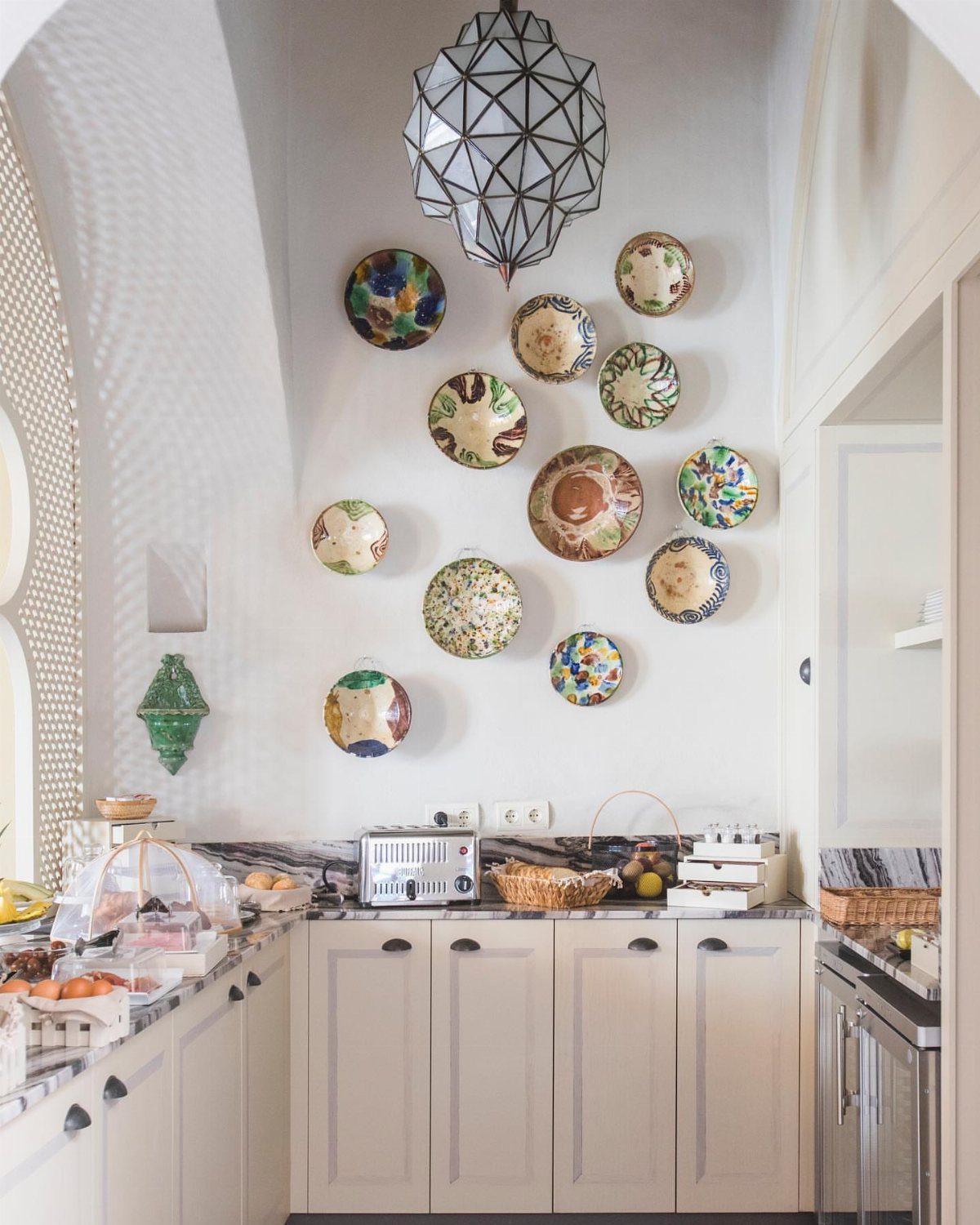 15 Small Breakfast Room Ideas for Cozy Spaces 7 White kitchen walls and cabinets decorated with colorful plates and a geometric lamp.