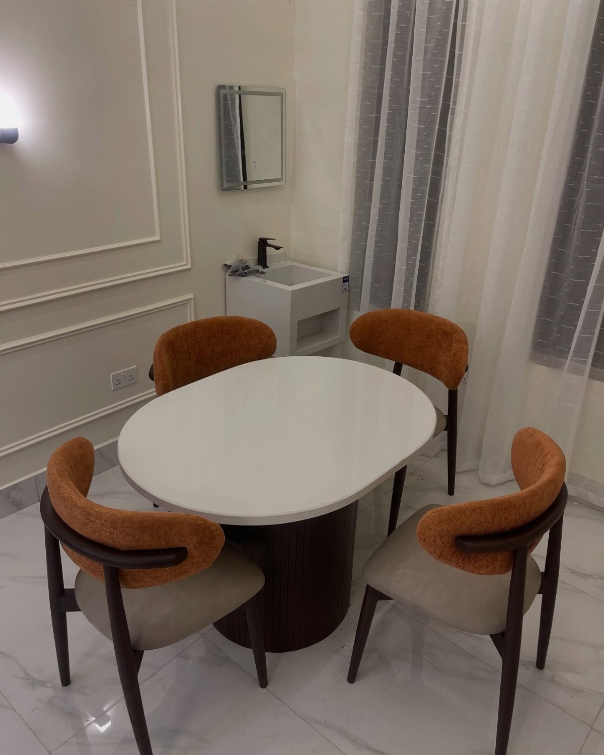 12 Small Dining Area Design Ideas That Maximize Space 9 White oval dining table with four orange and beige modern chairs in a bright room.