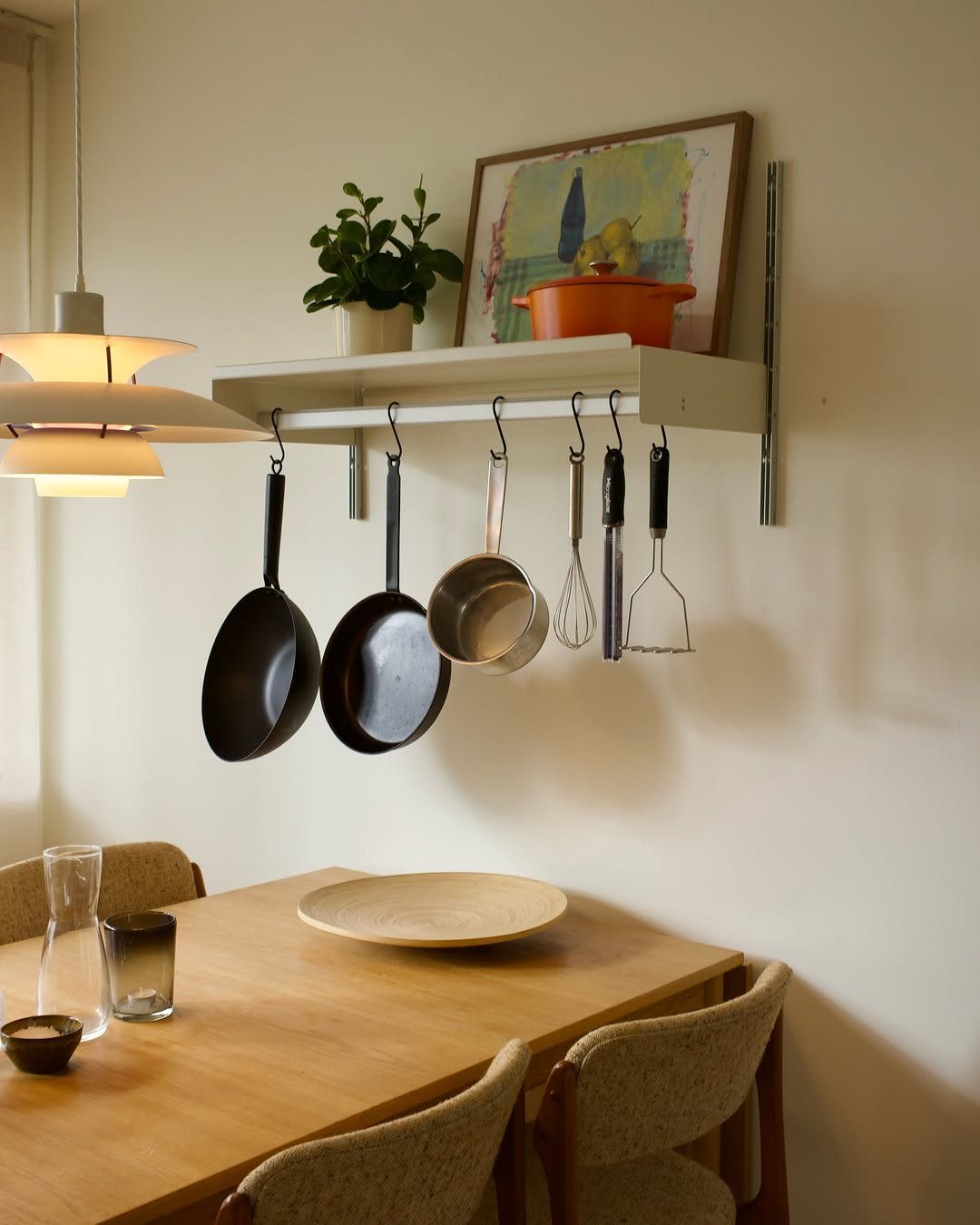 12 Small Dining Area Design Ideas That Maximize Space 7 Wall-mounted shelf with hanging pots and kitchen utensils above a wooden dining table.