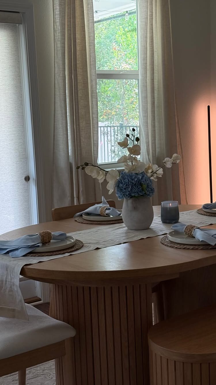 12 Small Dining Area Design Ideas That Maximize Space 6 Round wooden dining table with blue floral centerpiece and white curtains in background