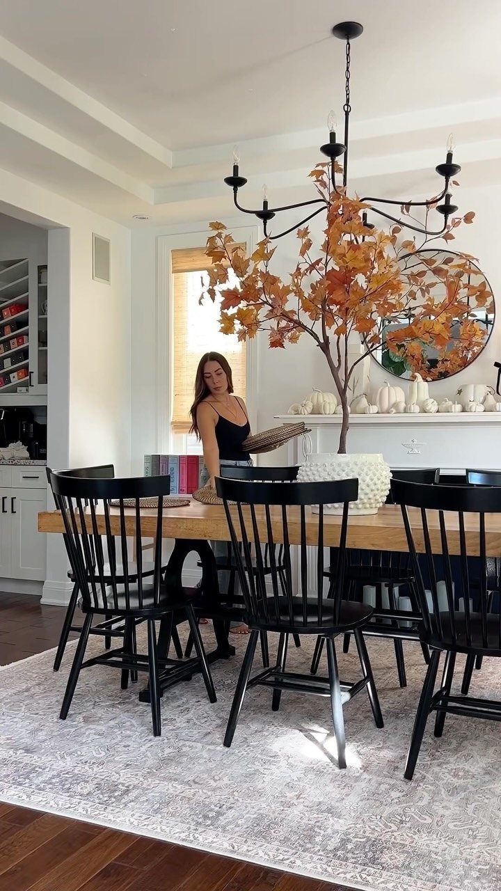 Light patterned rug under a wooden dining table with black chairs and autumn decor.