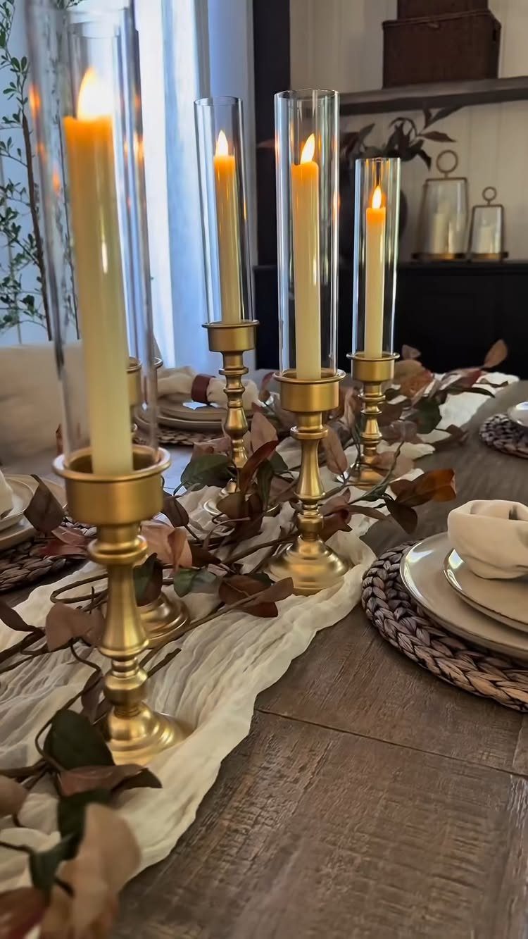 8 Small Dining Table Decor Ideas for Every Style 4 Gold candlesticks with lit yellow taper candles on a wooden dining table runner.