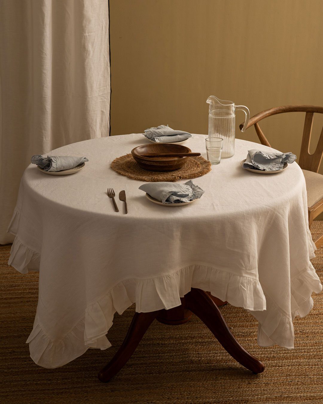 8 Small Dining Table Decor Ideas for Every Style 8 Round dining table with white ruffled tablecloth, wooden bowl, and blue napkins.